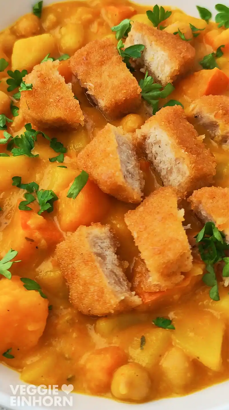 Nahaufnahme von klein geschnittenen veganen Nuggets auf einem Kürbis-Kichererbseneintopf.