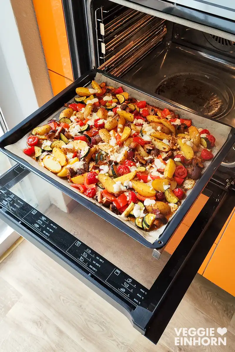 Mediterranes Blechgemüse mit Drillingen und veganem Feta auf dem Backblech im geöffneten Ofen.