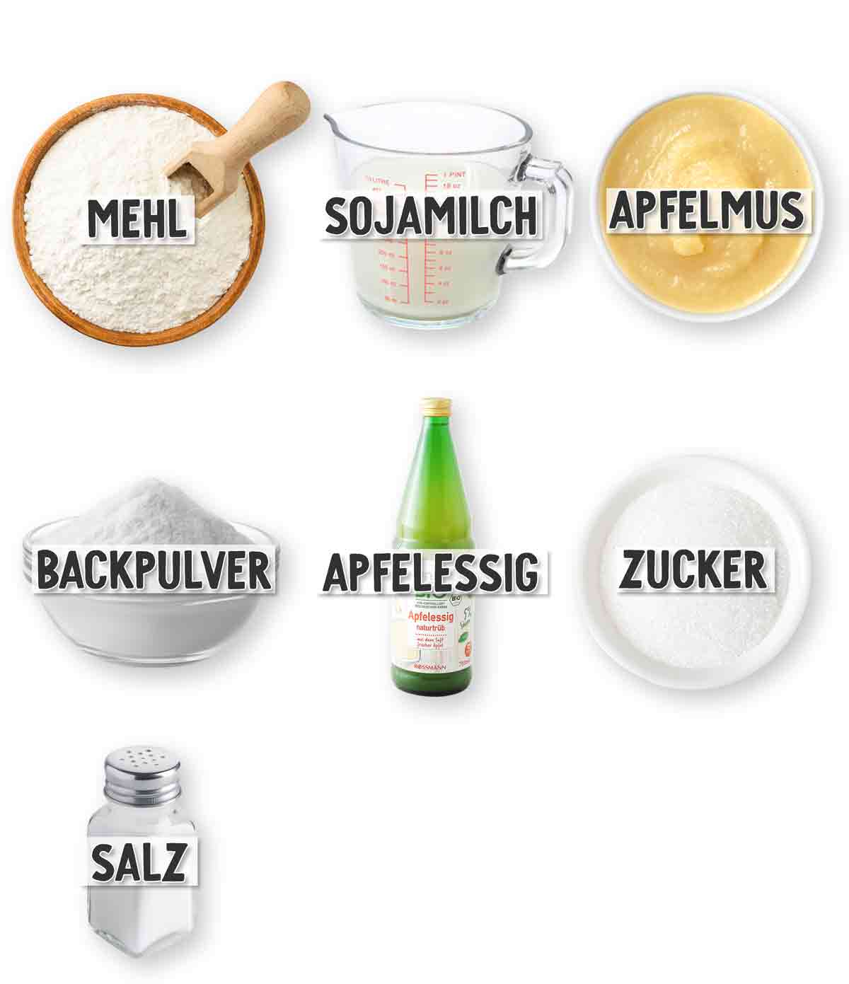 Zutaten für fluffige vegane Pancakes: Mehl in einer Holzschale mit Holzlöffel, Sojamilch in einem Messbecher, Apfelmus in einer Schale, Backpulver in einer kleinen Schüssel, eine Flasche Apfelessig, Zucker in einer weißen Schale und Salz. Jede Zutat ist mit einem beschrifteten Etikett versehen.