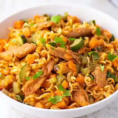 Weißer Teller mit Mie Nudeln, veganem Hähnchen, Salatgurke, Möhren, Frühlingszwiebeln.
