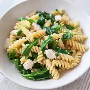 Pasta mit Rucola und zerbröseltem veganem Feta in einem weißen Teller serviert.