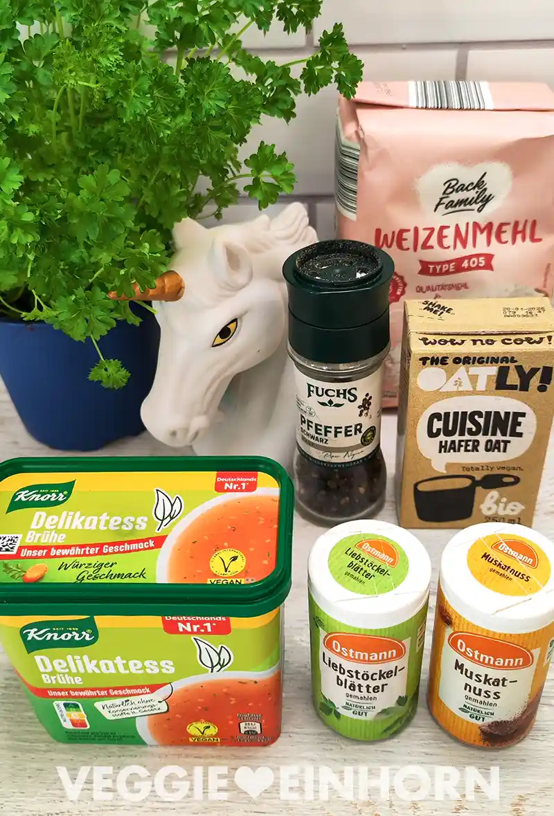 Frische Petersilie in einem Blumentopf steht neben einer Einhornfigur. Daneben liegen Zutaten wie Weizenmehl, schwarze Pfefferkörner, Hafer-Cuisine von Oatly, Delikatess-Gemüsebrühe, gemahlene Liebstöckelblätter und Muskatnuss von Ostmann.