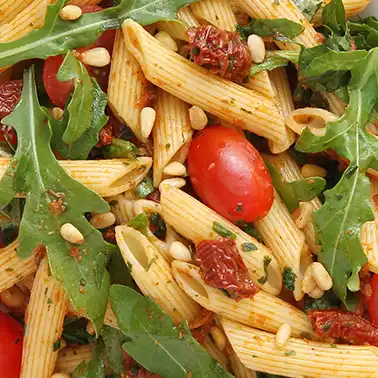 Veganer Nudelsalat mit Rucola, Kirschtomaten, getrockneten Tomaten und Pinienkernen als Symbolbild für die Kategorie Rezepte für vegane Nudelsalate.