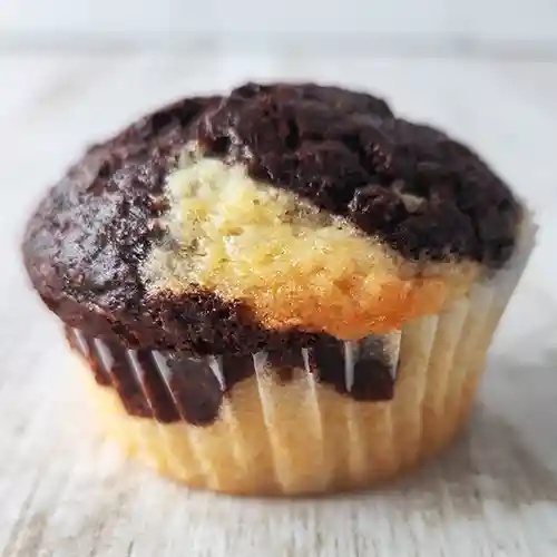 Ein veganer Marmormuffin mit Schokoladenteig und Vanilleteig in einer weißen Papierform auf einem hellen Holztisch.