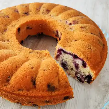 Saftiger veganer Blaubeerkuchen in Rohrbodenform mit herausgeschnittenem Stück.