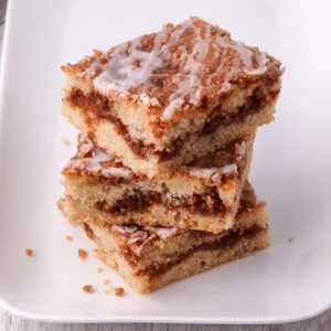 Saftige Zimtkuchenstücke mit Zuckerguss übereinandergestapelt auf einem weißen Teller.