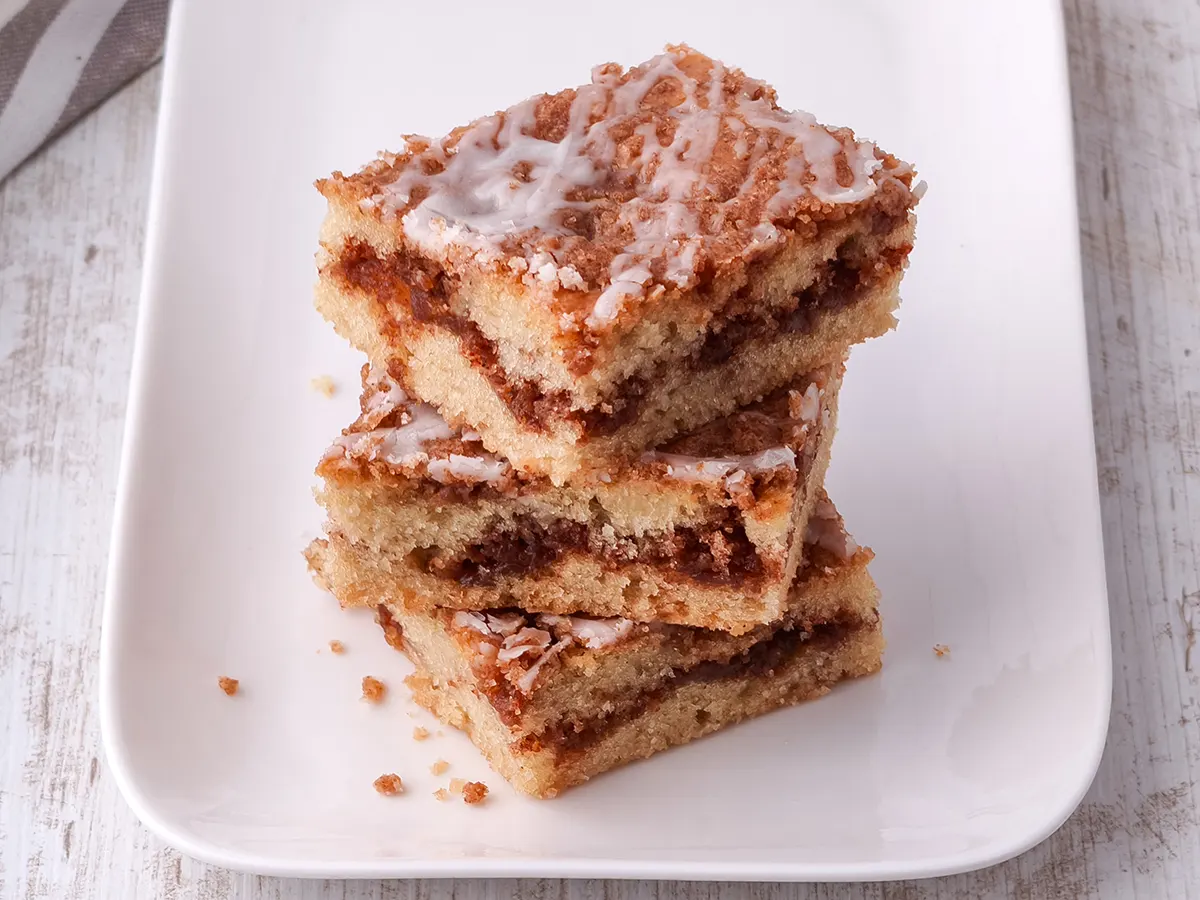 Saftige Zimtkuchenstücke mit Zuckerguss übereinandergestapelt auf einem weißen Teller.