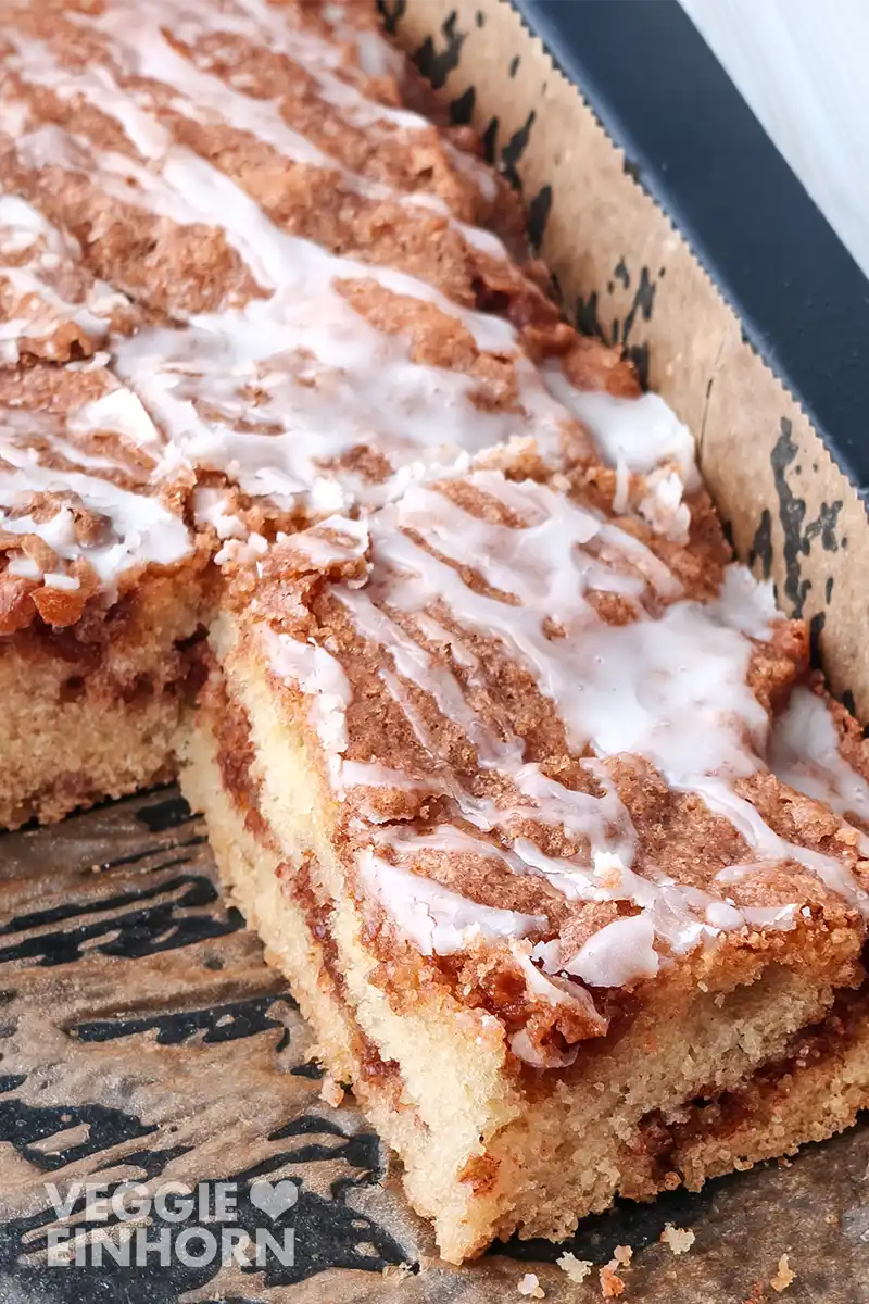 Nahaufnahme eines angeschnittenen Zimtkuchens mit Zuckerguss auf dem Backblech.