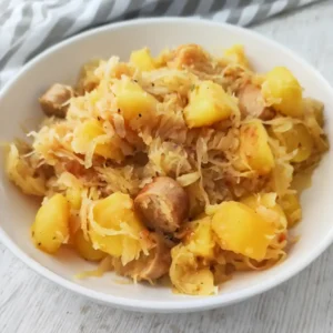 Eine Portion Sauerkraut-Kartoffelpfanne mit veganer Bratwurst auf einem Teller.