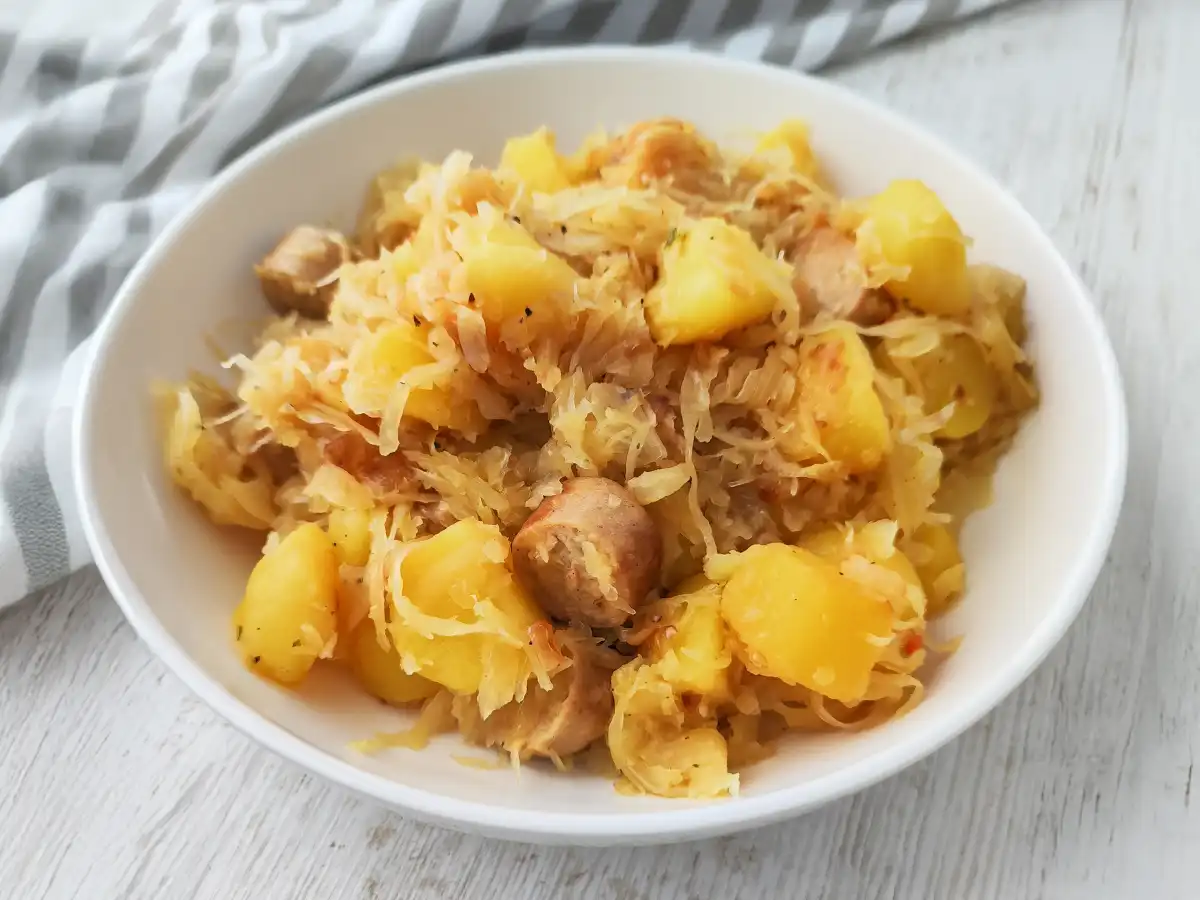 Eine Portion Sauerkraut-Kartoffelpfanne mit veganer Bratwurst auf einem Teller.