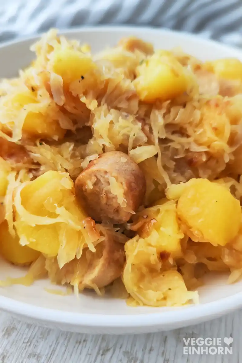 Vegane Kartoffel Bratwurst Pfanne mit Sauerkraut auf einem weißen Teller.