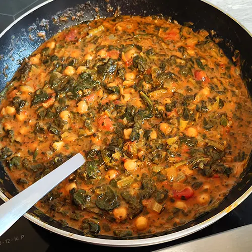 Veganes Curry mit Spinat, Kichererbsen und Kokosmilch in einer Pfanne mit Servierlöffel.