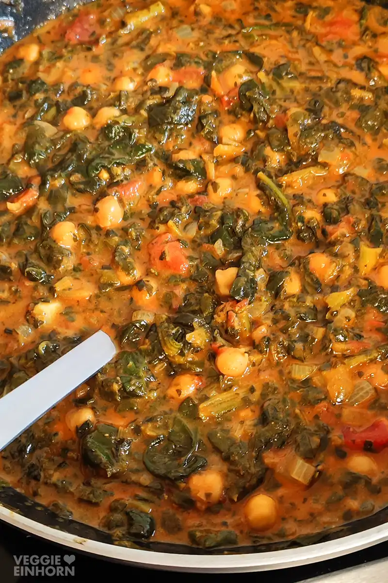 Nahaufnahme von einem Curry aus Spinat, Kichererbsen, Tomaten und Kokosmilch in einer Pfanne.