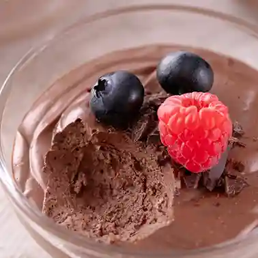 Vegane Mousse au Chocolat aus Seidentofu in einem Glasschälchen, dekoriert mit frischen Blaubeeren und einer Himbeere.