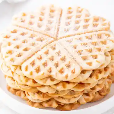 Ein Stapel veganer Waffeln auf einem weißen Teller, mit etwas Puderzucker bestäubt.