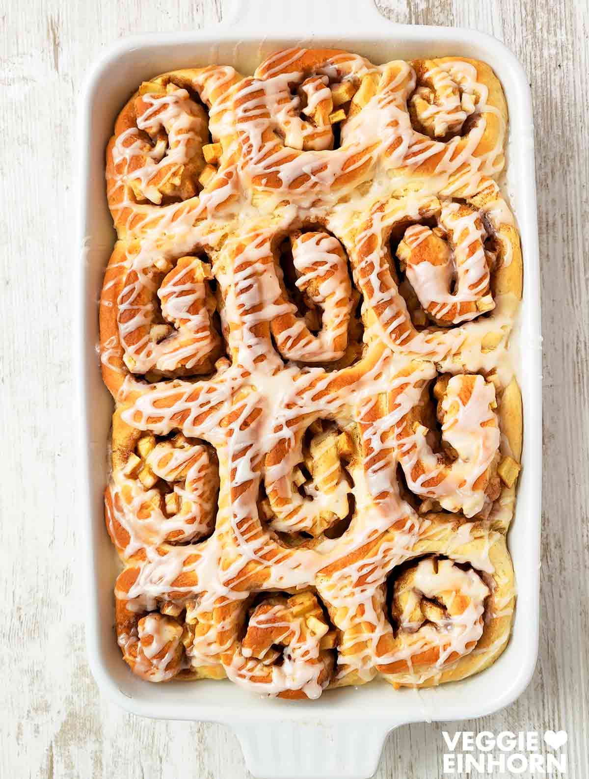 Frisch gebackene vegane Apfel-Zimt-Schnecken in einer weißen Auflaufform mit Zuckerguss.
