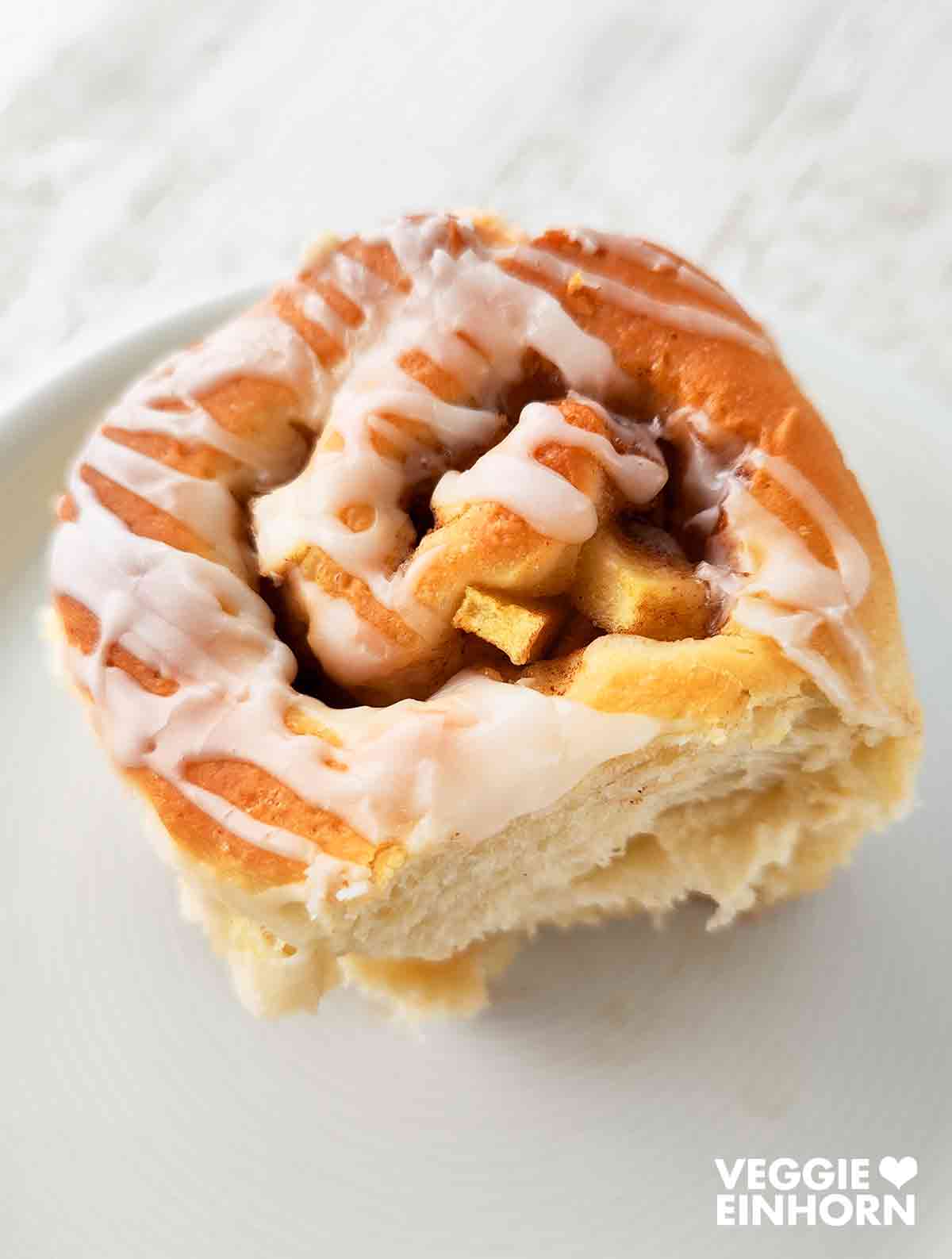 Einzelne vegane Apfel-Zimt-Schnecke auf einem weißen Teller, bestrichen mit Zuckerguss.
