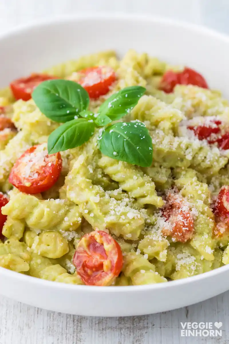 Ein Teller vegane Avocado Nudeln mit Kirschtomaten, bestreut mit veganem Parmesan und dekoriert mit frischem Basilikum.