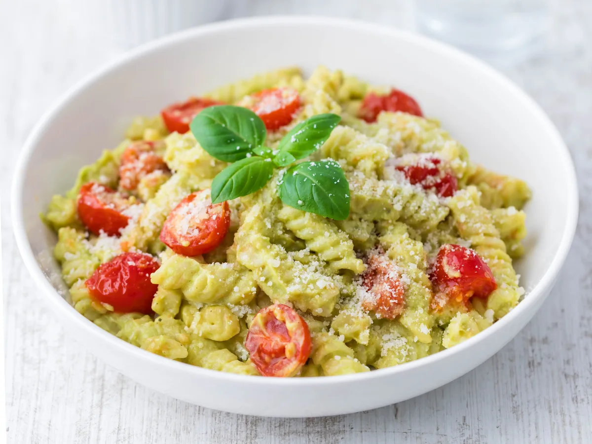 Vegane Avocado Pasta mit Kirschtomaten, bestreut mit veganem Parmesan und dekoriert mit frischem Basilikum.