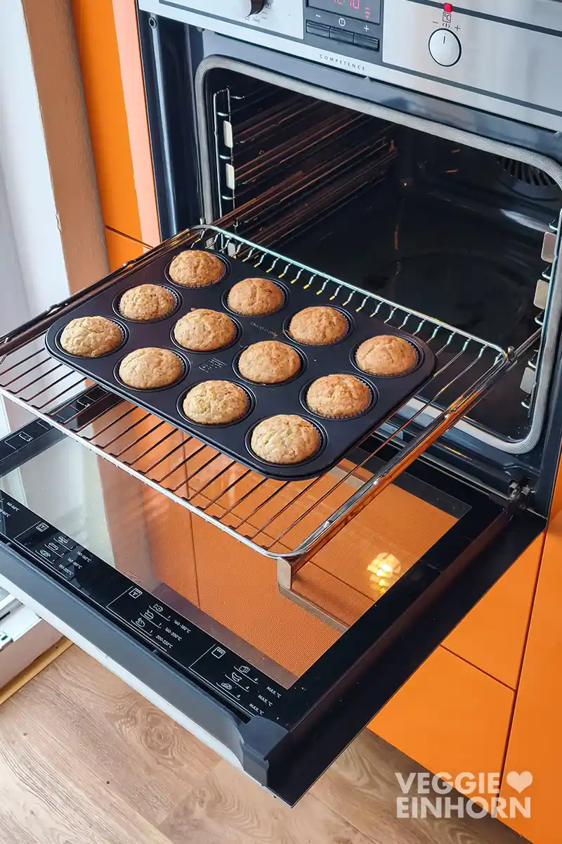 Muffinblech mit veganen Bananenbrot Muffins im geöffneten Backofen auf einem Auszugrost.