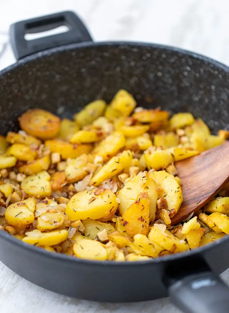 Vegane Bratkartoffeln mit Räuchertofu in einer Pfanne, goldgelb gebraten mit Zwiebeln.