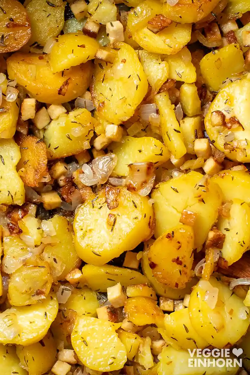 Nahaufnahme von veganen Bratkartoffeln mit Räuchertofu und Zwiebeln, goldbraun gebraten.