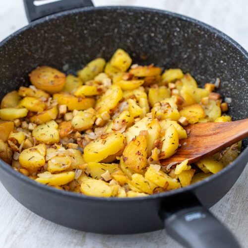 Vegane Bratkartoffeln mit Räuchertofu und Zwiebeln, goldbraun gebraten in einer Pfanne.