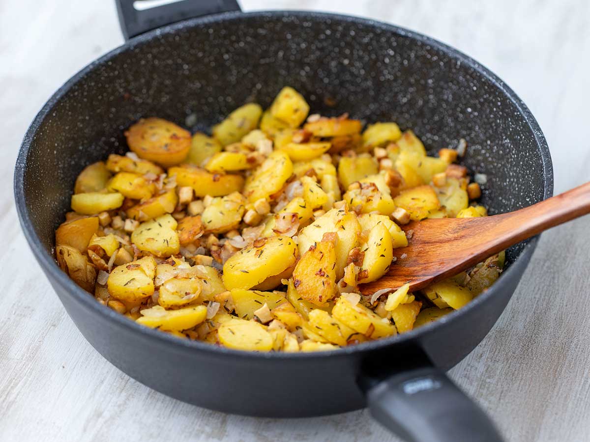 Vegane Bratkartoffeln mit Räuchertofu und Zwiebeln, goldbraun gebraten in einer Pfanne.