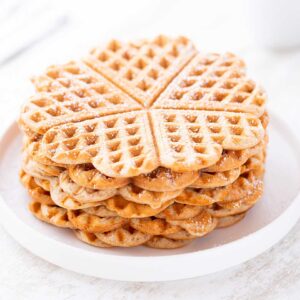 Gestapelte vegane Dinkelwaffeln auf einem weißen Teller, leicht bestäubt mit Puderzucker.