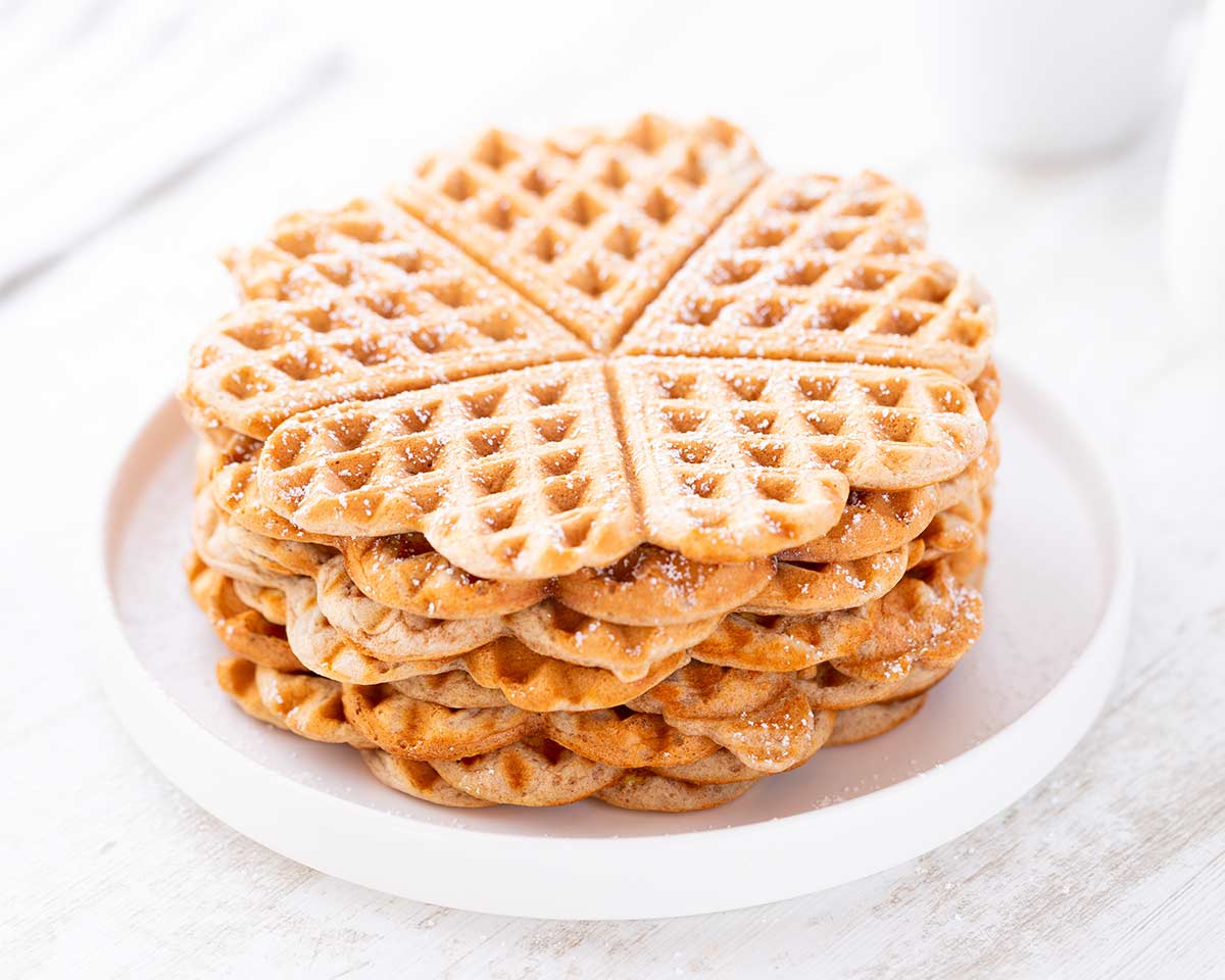 Gestapelte vegane Dinkelwaffeln auf einem weißen Teller, leicht bestäubt mit Puderzucker.