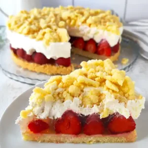 Angeschnittene vegane Erdbeertorte mit Streuseln und Sahne, davor ein Teller mit einem Tortenstück.