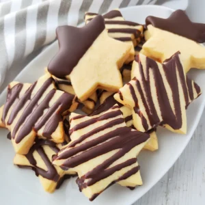 Vegane gefüllte Orangenplätzchen in Sternform liegen auf einem weißen Teller und sind mit dunkler Schokolade verziert.