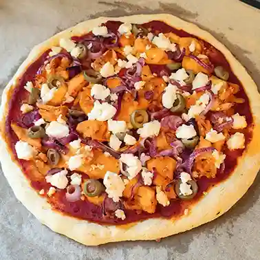 Frisch gebackene vegane Gyrospizza mit Pizzasauce, veganen Gyrosstücken, roten Zwiebeln, Oliven und veganem Feta auf Backpapier.