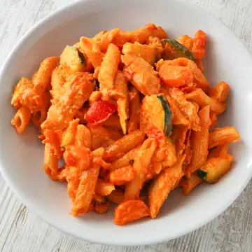 Cremige vegane Hähnchenpfanne mit Penne, Zucchini, Möhren und Tomaten.