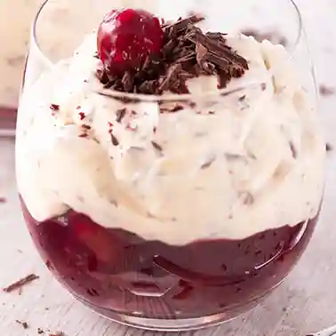 Vegane Herrencreme im Glas mit einer unteren Schicht aus Kirschen, darüber eine Schicht Sahnecreme, garniert mit Schokoladenraspeln und einer Kirsche.