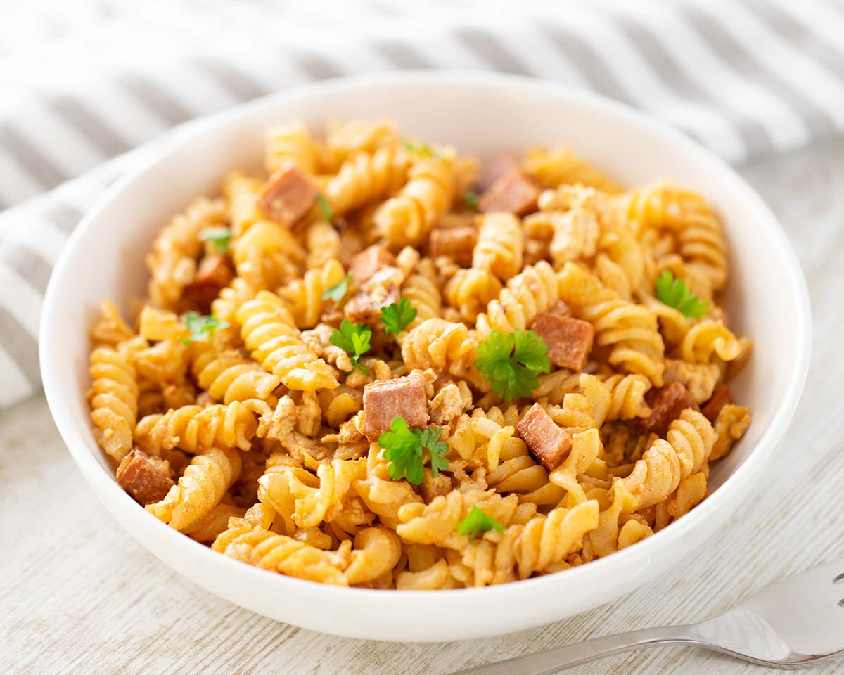 Nudeln mit veganem Leberkäse, serviert auf einem weißen Teller und mit Petersilie dekoriert.