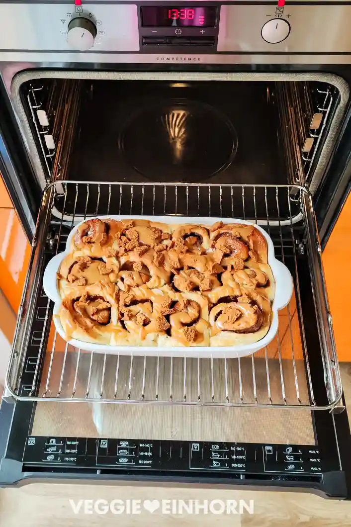 Weiße Auflaufform mit frisch gebackenen veganen Lotus Zimtschnecken im geöffneten Backofen. 