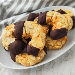 Vegane Mandelhörnchen auf einem weißen Teller, mit Mandelblättchen bedeckt und in dunkle Schokolade getaucht.