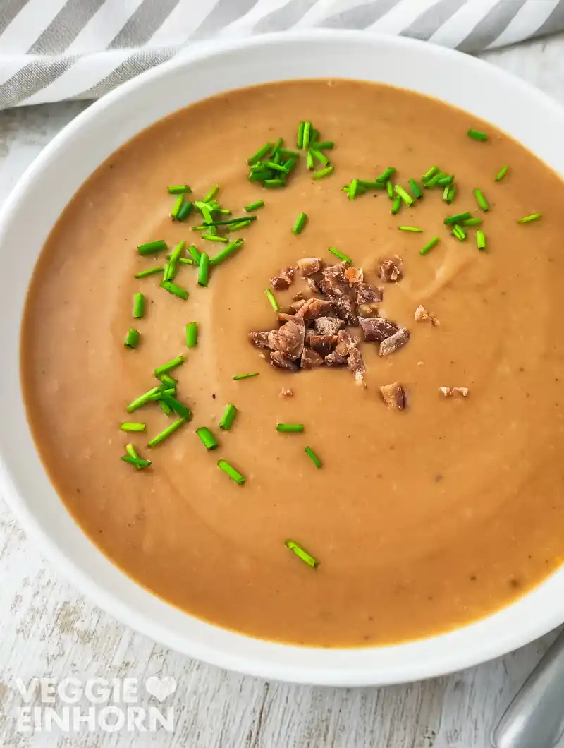 Nahaufnahme von cremiger veganer Maronen-Kartoffelsuppe, garniert mit Schnittlauchröllchen und Maronenstückchen.