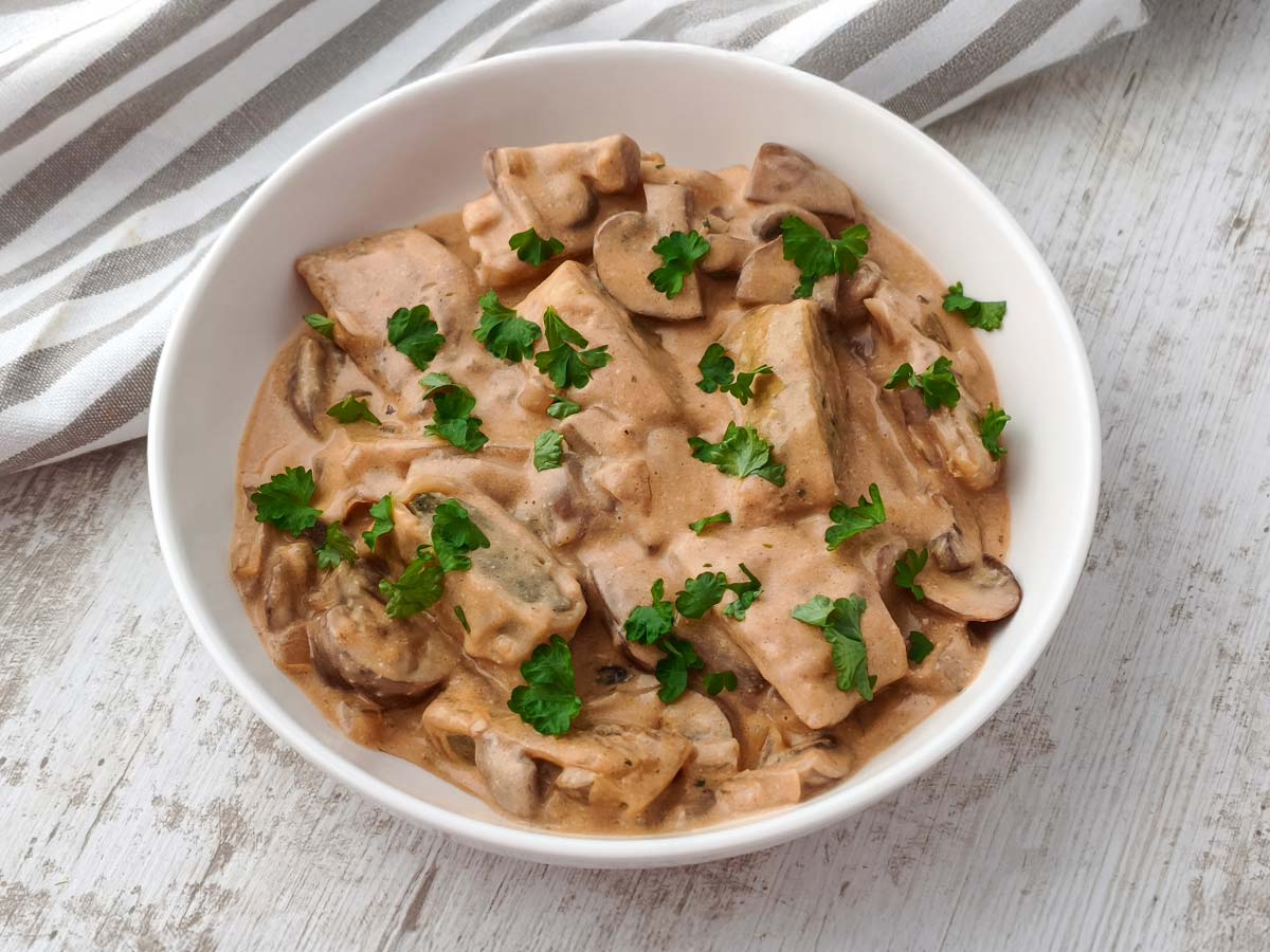 Vegane Maultaschen in Champignon Rahmsoße mit Petersilie auf einem weißen Teller.