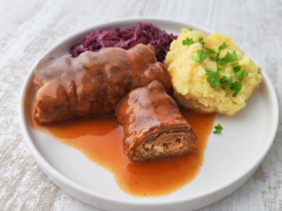 Vegane Roulade aus Soja Big Steaks mit Bratensoße auf einem Teller mit Kartoffelpüree und Rotkohl.