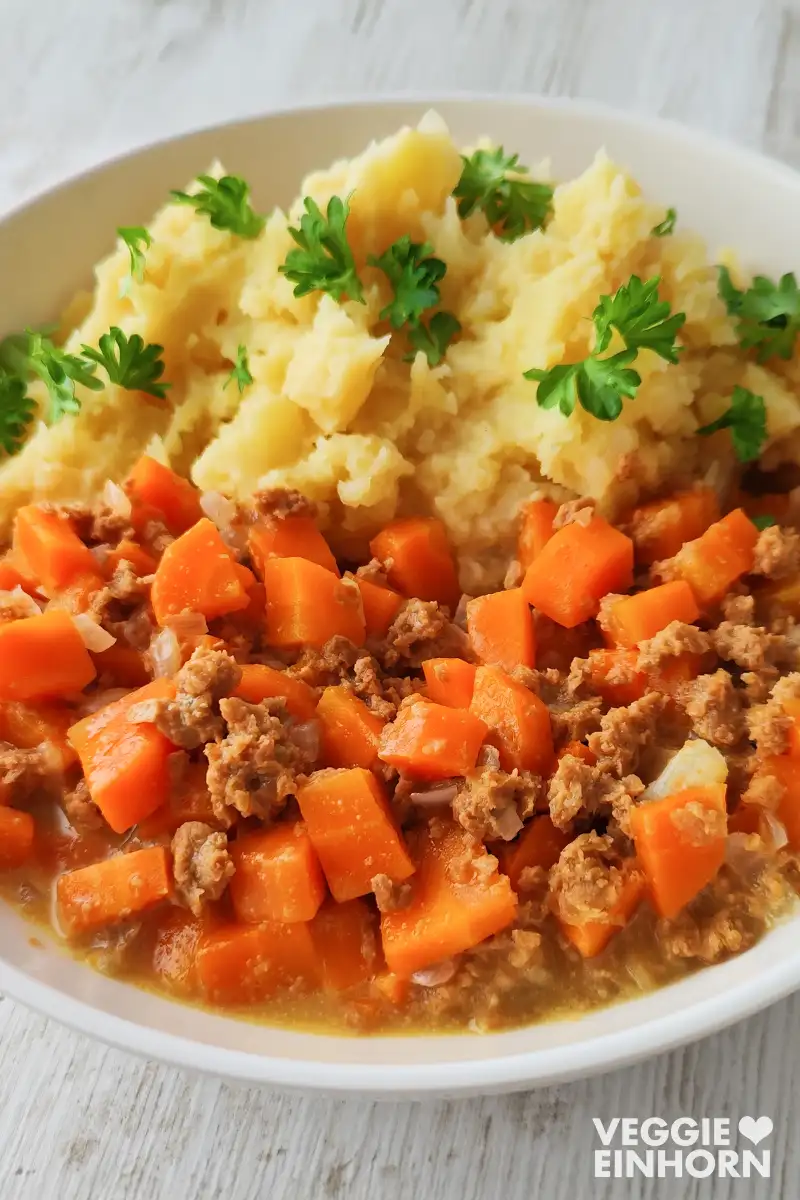 Sahne-Möhren mit veganem Hackfleisch neben einem cremigen Kartoffelbrei, angerichtet auf einem weißen Teller.