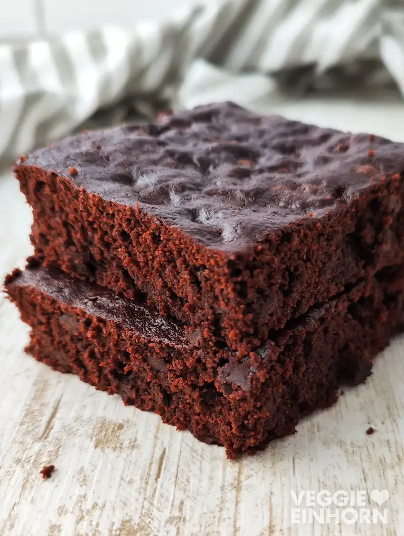 Zwei saftige vegane Schokobrownies auf hellem Holztisch in Nahaufnahme.