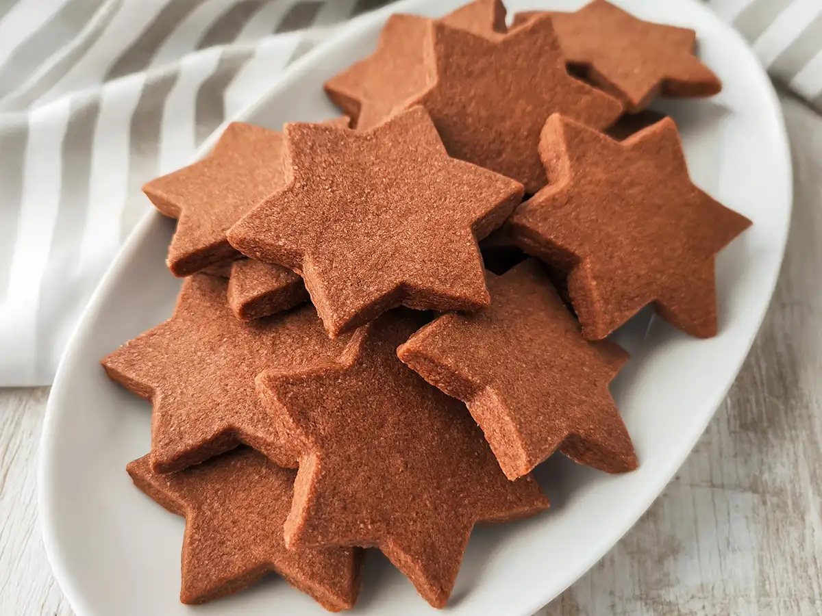 Vegane Schokoplätzchen in Sternform liegen auf einem weißen Plätzchenteller.