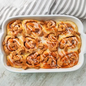 Vegane Spekulatius-Zimtschnecken mit Spekulatiusstückchen und Zuckerguss in einer weißen Auflaufform.