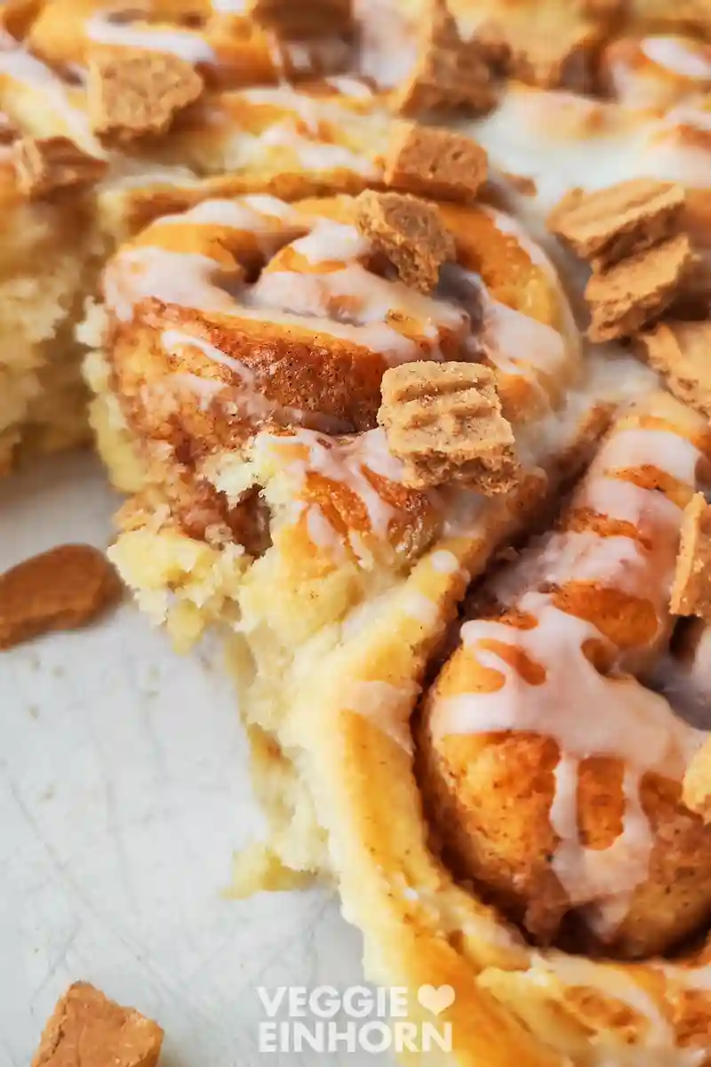 Nahaufnahme von veganen Spekulatius-Zimtschnecken in der Auflaufform, es wurden schon einige Schnecken entnommen und die fluffige Textur ist sichtbar.
