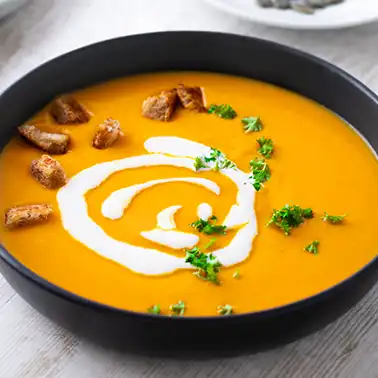 Vegane Kürbissuppe in einer schwarzen Schale als Symbolbild für die Kategorie Rezepte für vegane Suppen.