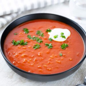 Schwarzer Teller mit veganer Tomatensuppe mit Reis, garniert mit frischer Petersilie und einem Klecks veganer Créme fraîche.