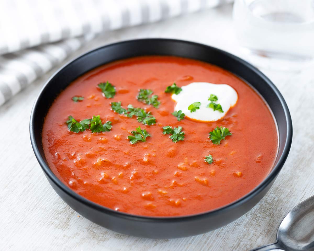 Schwarzer Teller mit veganer Tomatensuppe mit Reis, garniert mit frischer Petersilie und einem Klecks veganer Créme fraîche.