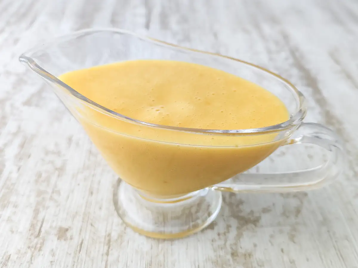 Vegane Vanillesoße in einer gläsernen Sauciere auf einem hellem Holztisch.